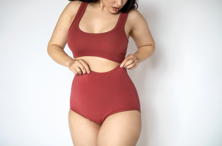 Frau in roter Unterwäsche berührt ihren Bauch, Nahaufnahme der Körpermitte vor hellem Hintergrund